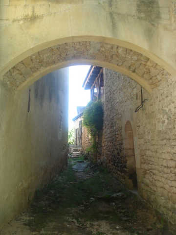 Photographie d'une ruelle étroite à Nozac avec une arche reliant deux maisons au premier plan.